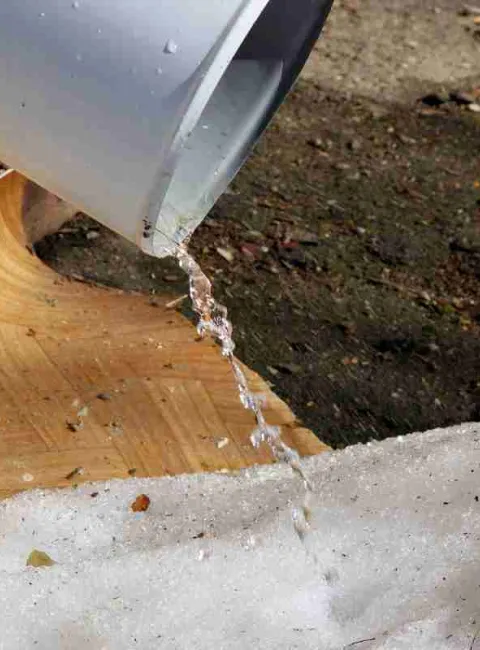 snow melt coming down a spout at a house