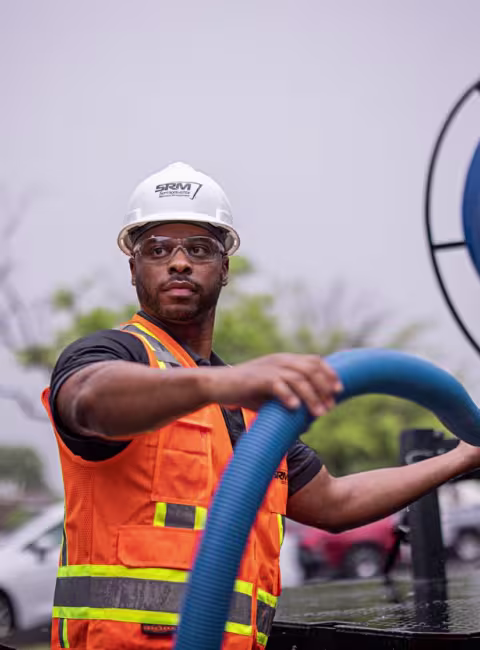 Worker coils thick blue hose outdoors carefully.