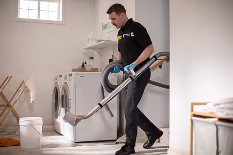 ServiceMaster technician carrying extraction wand and vacuum hose into effected water loss area