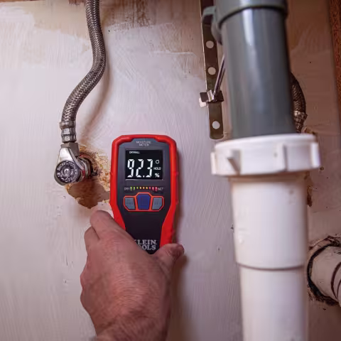 Using electronic moisture meter on wall under sink