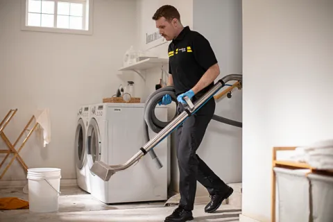 servicemaster tech carring wand and vacuum hose into an active water damage