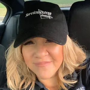 A woman smiling at the camera with short blonde hair. She is wearing a black ServiceMaster hat and matching polo.