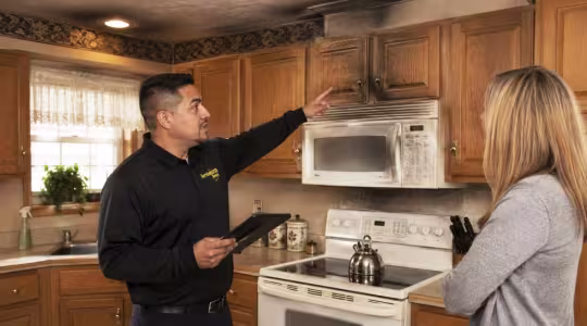ServiceMaster technician discussing the smoke damage cleanup process to a homeowner while standing in a smoke damaged kitchen